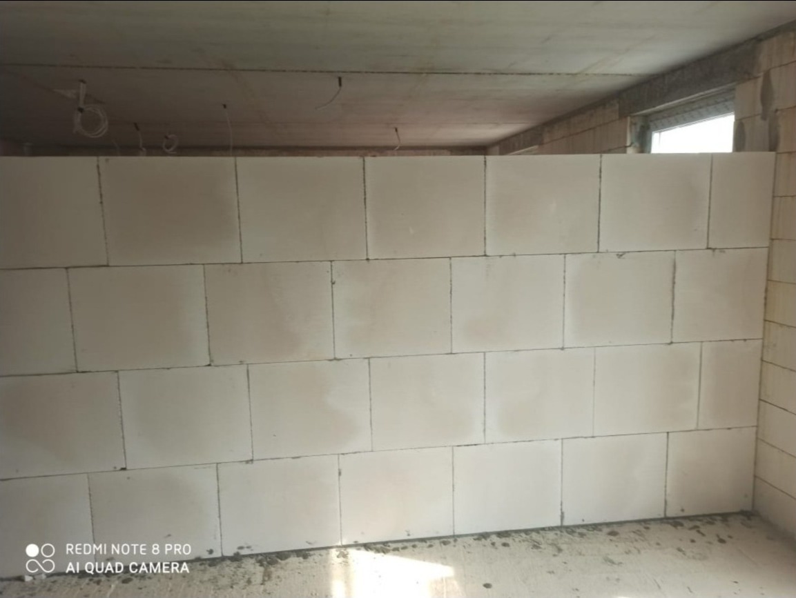 Wewnętrzna ściana działowa z białych bloczków, widoczne przewody elektryczne pod sufitem, surowy stan wykończenia.