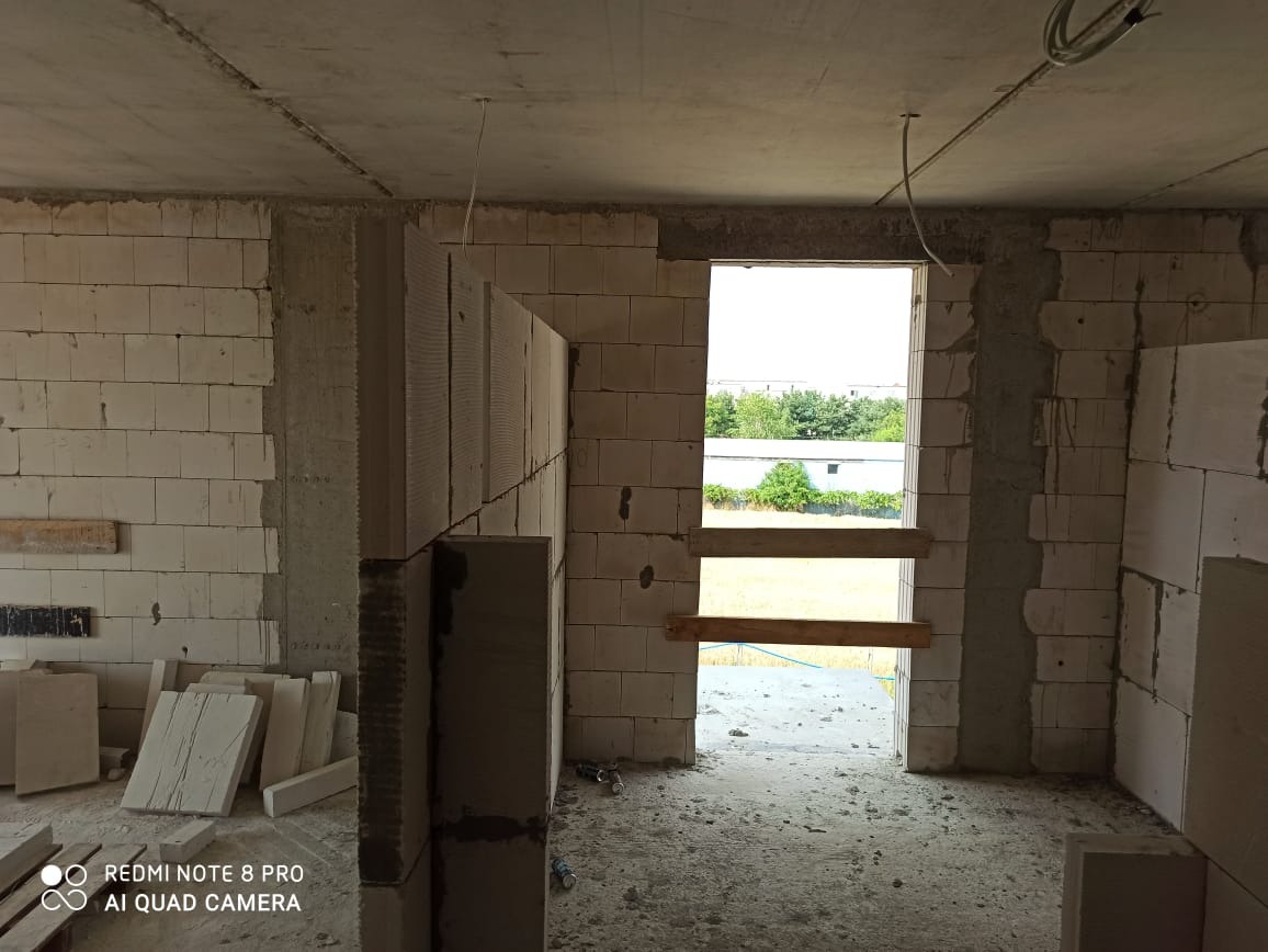 Wnętrze budynku w trakcie budowy z widocznymi bloczkami z betonu komórkowego i surowym betonowym sufitem, przygotowane do nałożenia warstwy tynku.