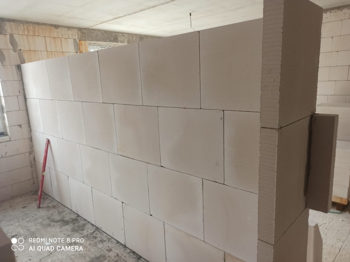 Wznoszenie ściany działowej z białych bloczków betonu komórkowego, widoczna poziomica oparta o ścianę, surowy stan wnętrza.