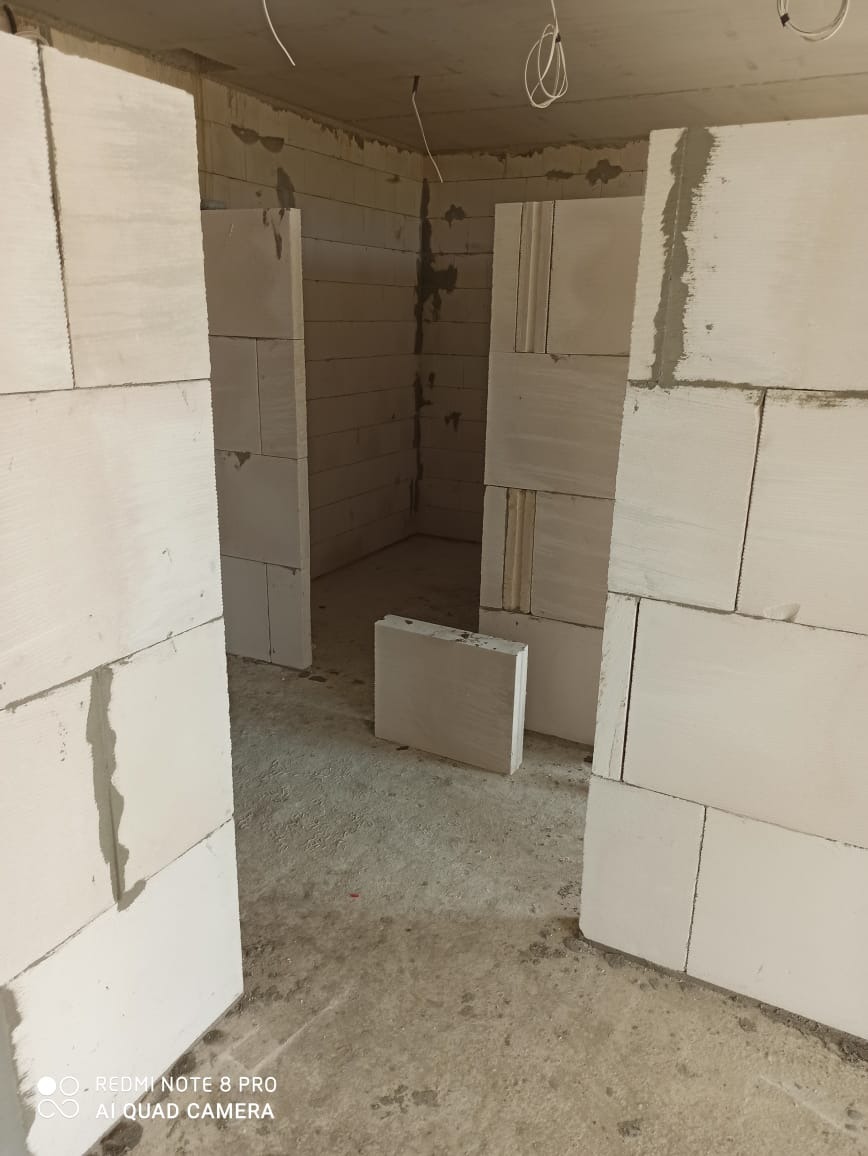 Wnętrze w trakcie budowy ścian działowych z betonu komórkowego; widoczne niedoskonałości w łączeniach i surowy beton na podłodze.