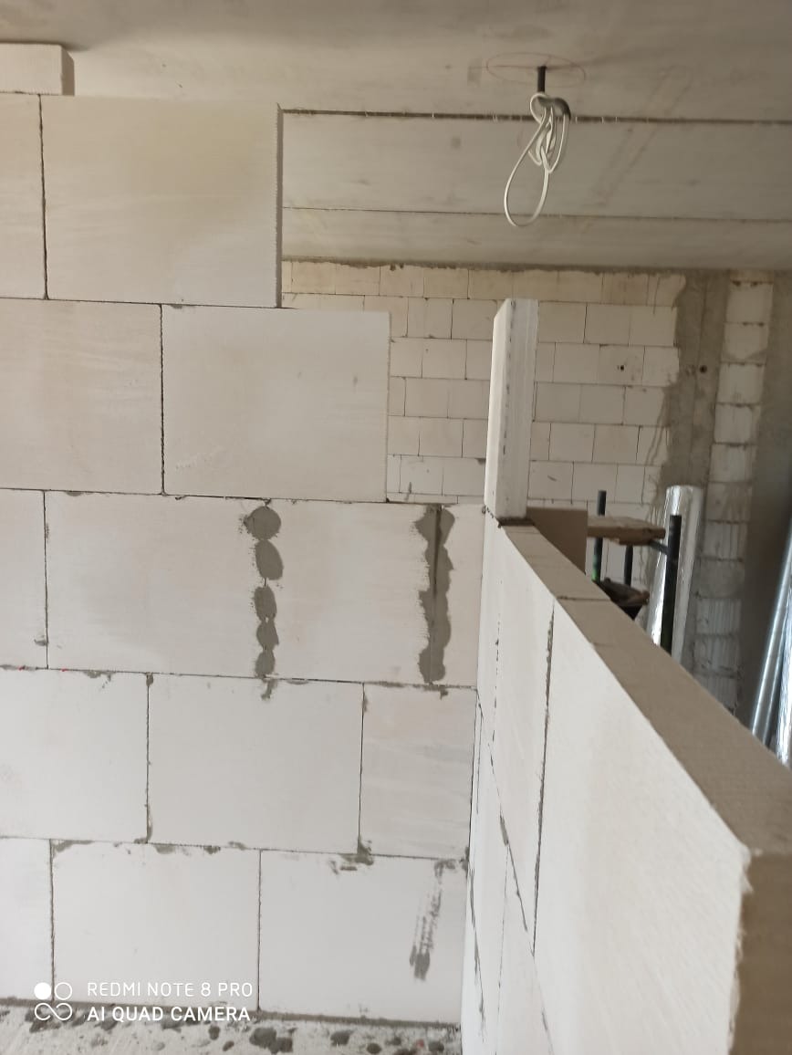 Wnętrze w trakcie budowy ściany z białych bloczków, widoczne ślady zaprawy i wystające kable z sufitu.