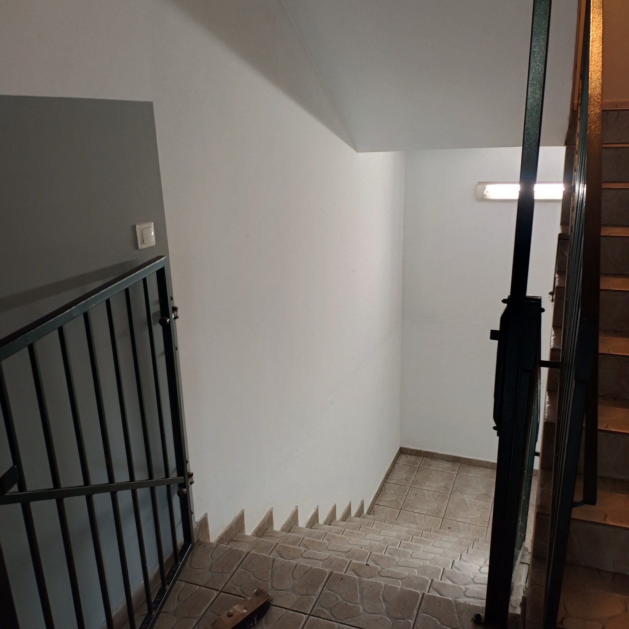 Klatka schodowa w budynku w Myśliborzu, z widocznymi schodami wyłożonymi płytkami, białą ścianą z włącznikiem światła i czarną metalową barierką.