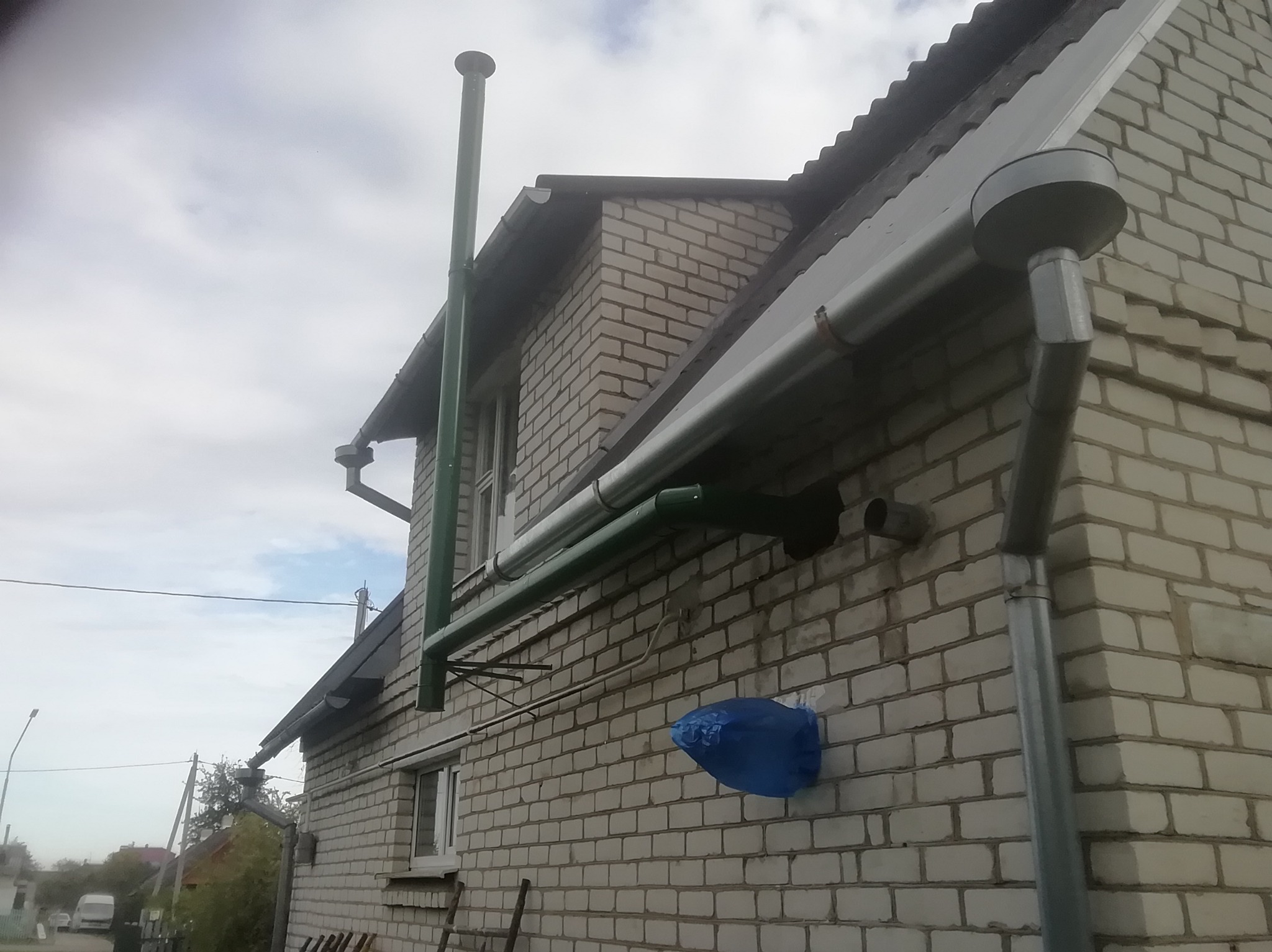 Dom z białej cegły z zamontowanymi rynnami w kolorze srebrnym i zielonym kominem, widok z dołu.