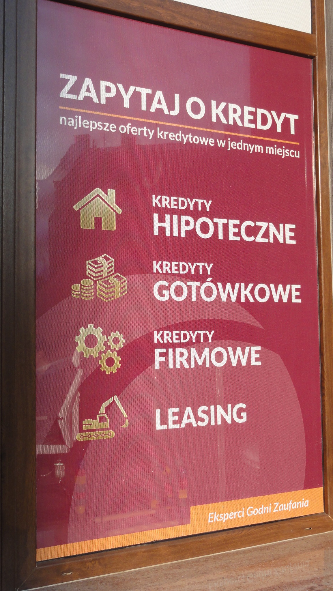 Plakat reklamowy w ramie z ofertami kredytowymi: hipoteczne, gotówkowe, firmowe oraz leasing. Ikony przedstawiają dom, stos monet, zębatki i koparkę. Napis: Zapytaj o kredyt, eksperci godni zaufania.
