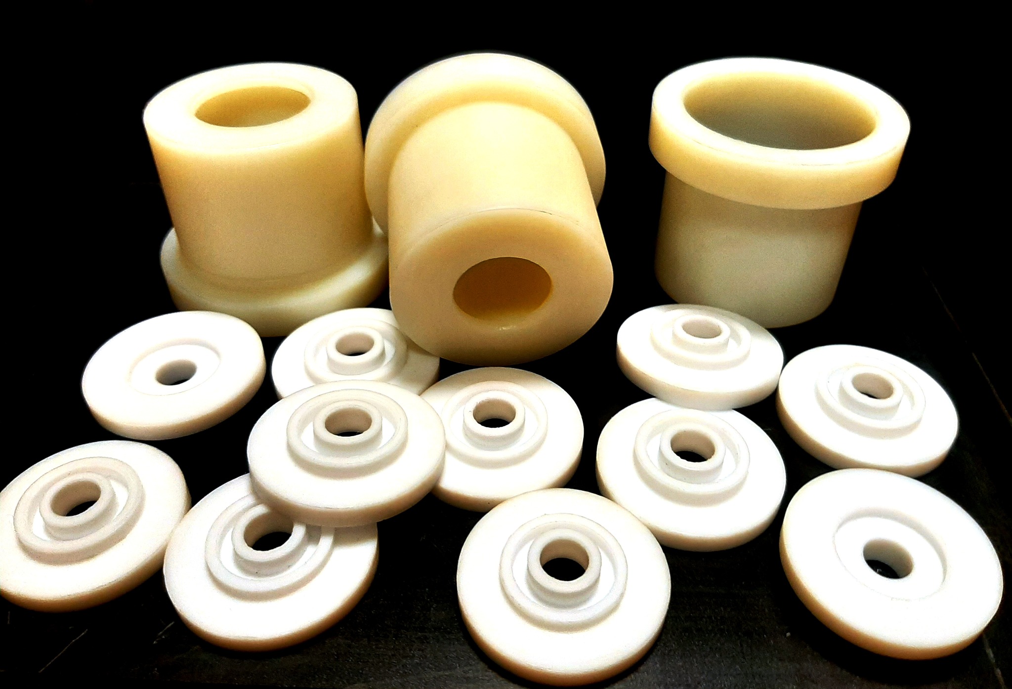 Precyzyjnie wykonane, kremowe elementy z tworzywa sztucznego o okrągłym kształcie, niektóre w formie tulei, inne jako podkładki, ułożone na ciemnym tle.