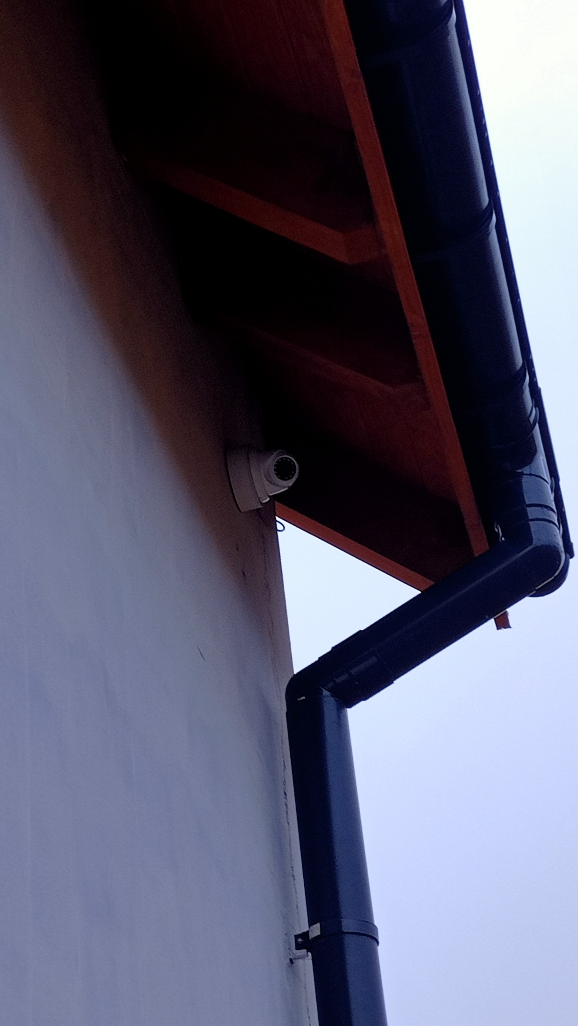 Kamera monitoringu zamontowana na elewacji budynku obok rynny spustowej, widok z dołu.