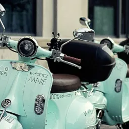 Szereg miętowych skuterów elektrycznych z napisem 'Wypożycz Mnie' i logo 'Eco Share.pl' zaparkowanych przy ulicznej latarni.