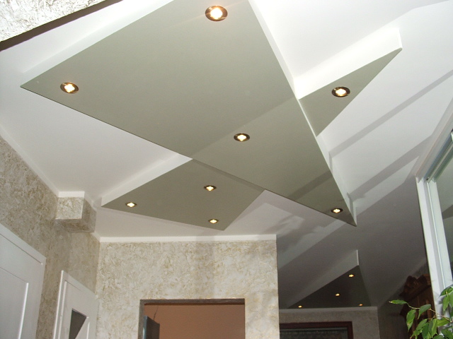 Nowoczesny sufit podwieszany z geometrycznymi panelami w odcieniach bieli i szarości, oświetlony punktowymi lampami LED, w pomieszczeniu z dekoracyjną tapetą.