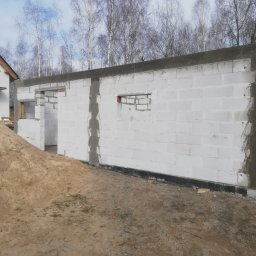 Firma ogólnobudowlana - Budowa ścian z bloczków betonu komórkowego w Połajewie, widoczny fragment domu w tle i pryzma piasku.