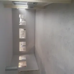 Wnętrze w trakcie wykańczania, ściany z widocznymi śladami po szpachlowaniu, przygotowane pod malowanie, z widocznymi otworami na instalacje.