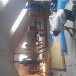 Pracownik w czapce przycina płytę na poddaszu, widoczne ocieplenie, drabina i okno dachowe.