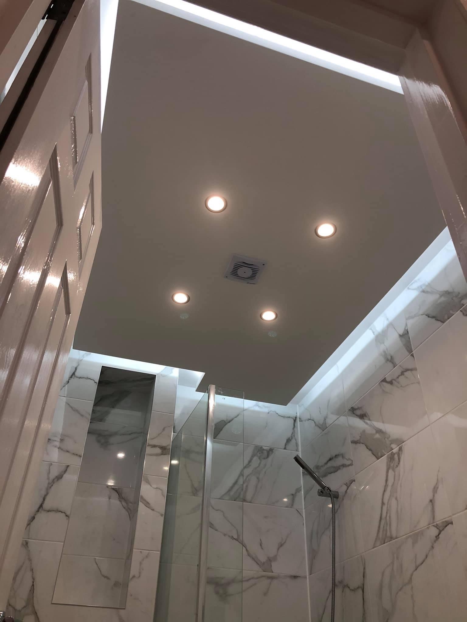 Wykończona łazienka z marmurowymi płytkami, kabiną prysznicową ze szklanymi ściankami, punktowym oświetleniem sufitowym i wentylatorem, widok z dołu.
