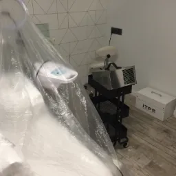 Przygotowane stanowisko pracy z lampą i wózkiem na akcesoria, przykryte folią ochronną, w tle ściana z geometrycznym wzorem i skrzynka z logo ITP Biomedical Company.