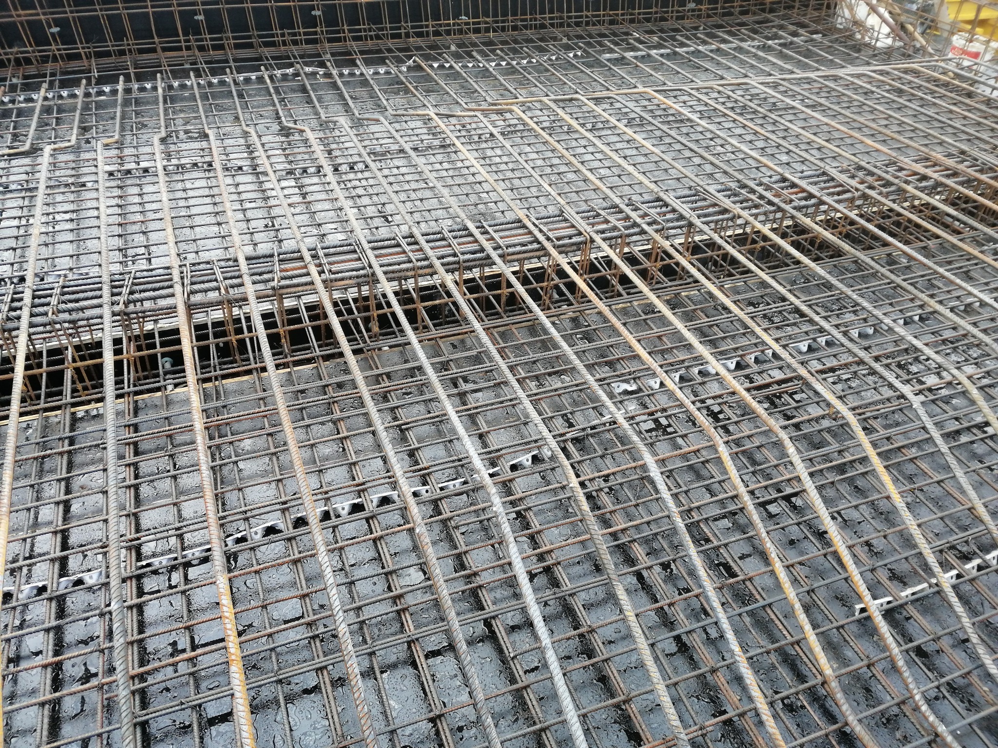 Zbrojenie płyty fundamentowej z widocznymi dystansami z tworzywa sztucznego, przygotowane do zalania betonem, mokra powierzchnia betonu.