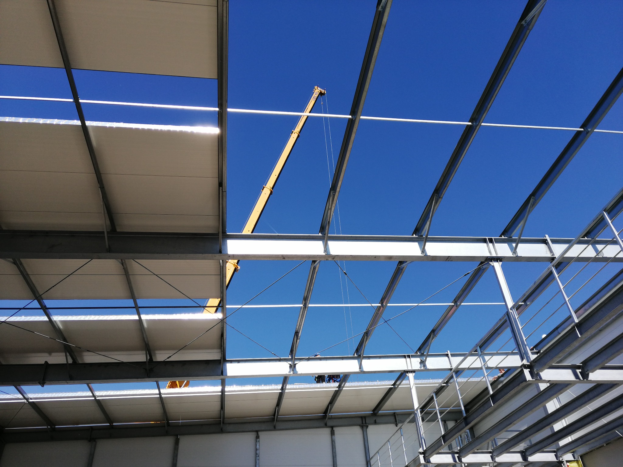 Montaż konstrukcji stalowej hali z widocznym dźwigiem na tle błękitnego nieba.