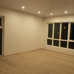 Puste, odświeżone wnętrze z panelami ściennymi, jasnymi płytkami podłogowymi imitującymi drewno, nowymi oknami i białymi listwami przypodłogowymi.