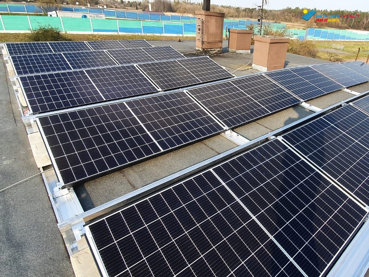 Instalacja fotowoltaiczna na płaskim dachu z widocznymi panelami, aluminiowymi konstrukcjami montażowymi i kominami wentylacyjnymi w tle.