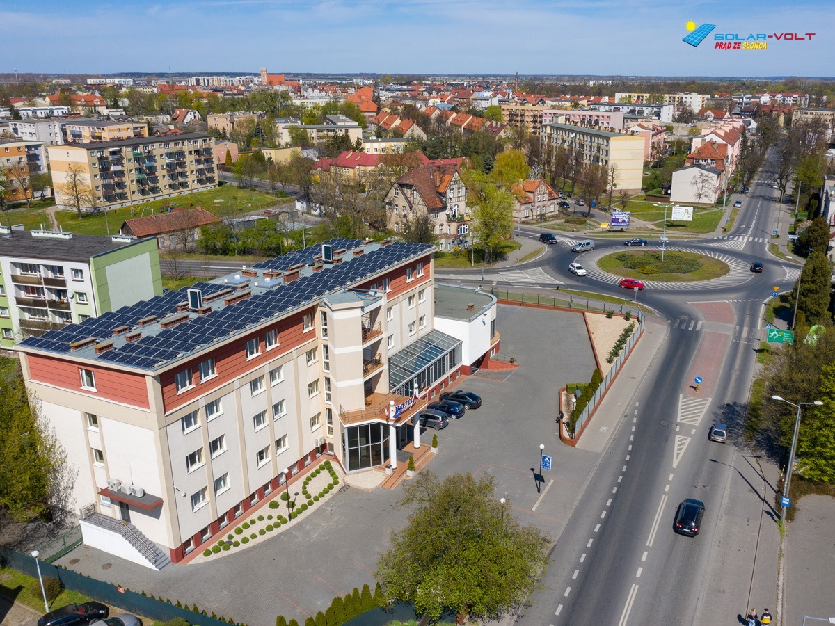 Widok z lotu ptaka na budynek z panelami słonecznymi na dachu, z widocznym rondem i otoczeniem miejskim w tle.