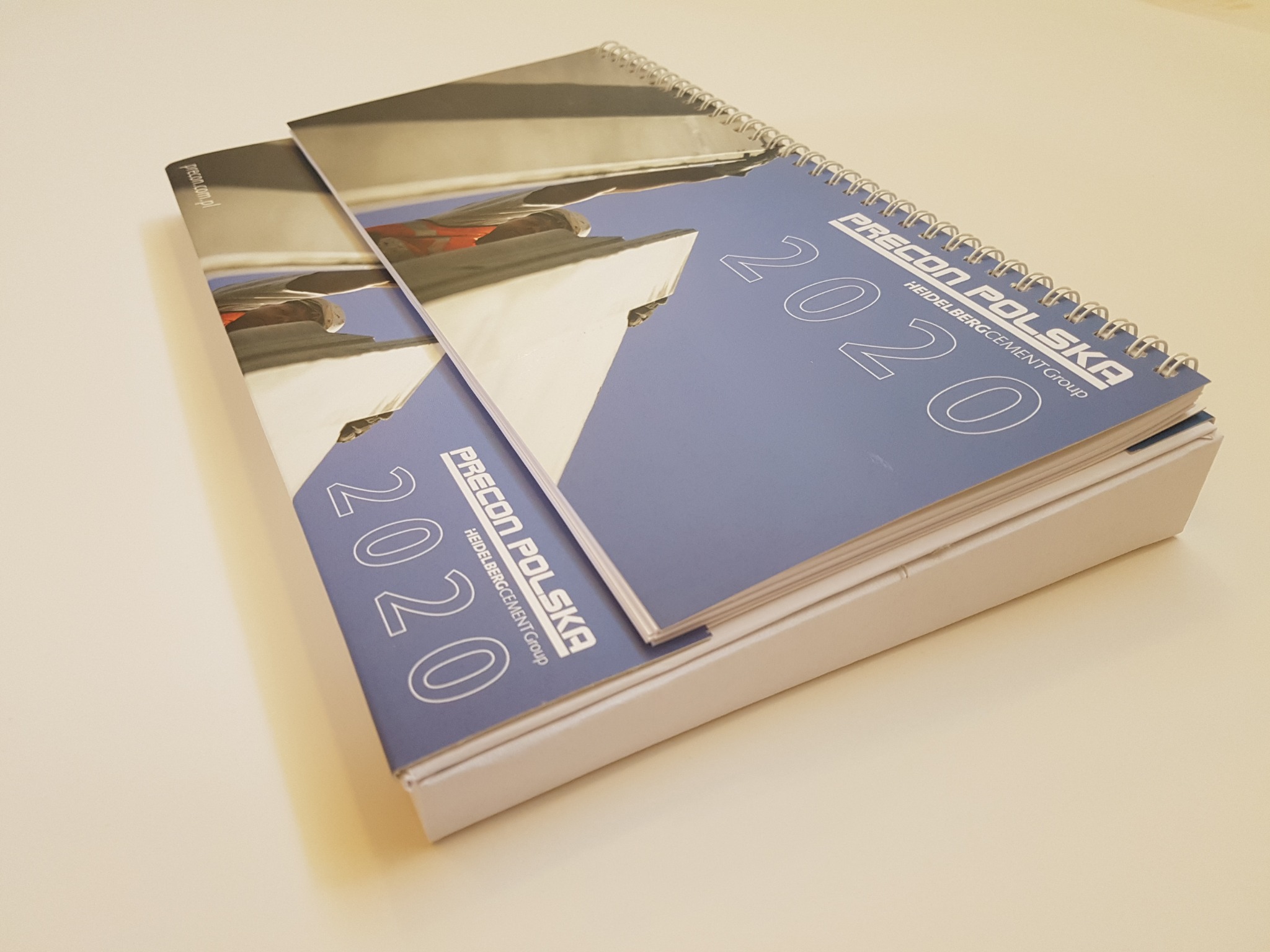 Dwa kalendarze biurkowe w formie piórnika z logo firmy Precon Polska i rokiem 2020, leżące na białym tle.