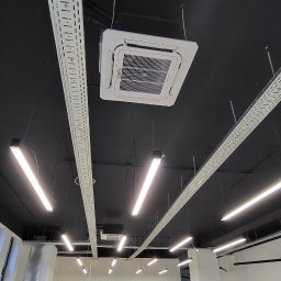 Longman Cooling & Heating - Sufit biurowy z zainstalowaną kasetonową klimatyzacją, widoczne koryta kablowe i oświetlenie liniowe. W tle surowy stan wykończenia pomieszczenia biurowego.