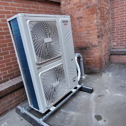 Longman Cooling & Heating - Zewnętrzna jednostka klimatyzacji Sinclair SDV z dwoma wentylatorami, zamontowana na metalowej konstrukcji na tle ceglanego budynku z oknami.