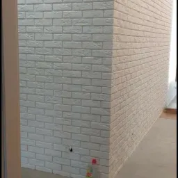 Ściana wykończona białą cegłą dekoracyjną, widoczny narożnik i fragment podłogi, przy ścianie stoi butelka środka czyszczącego.