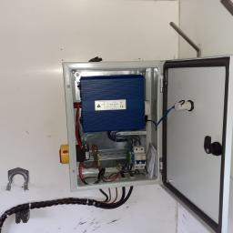 Control-Team Bartłomiej Glapiak - Otwarta skrzynka elektryczna z niebieskim modułem sterującym IPS-1000S DUO, widoczne przewody, bezpieczniki i wyłącznik awaryjny na białej ścianie.