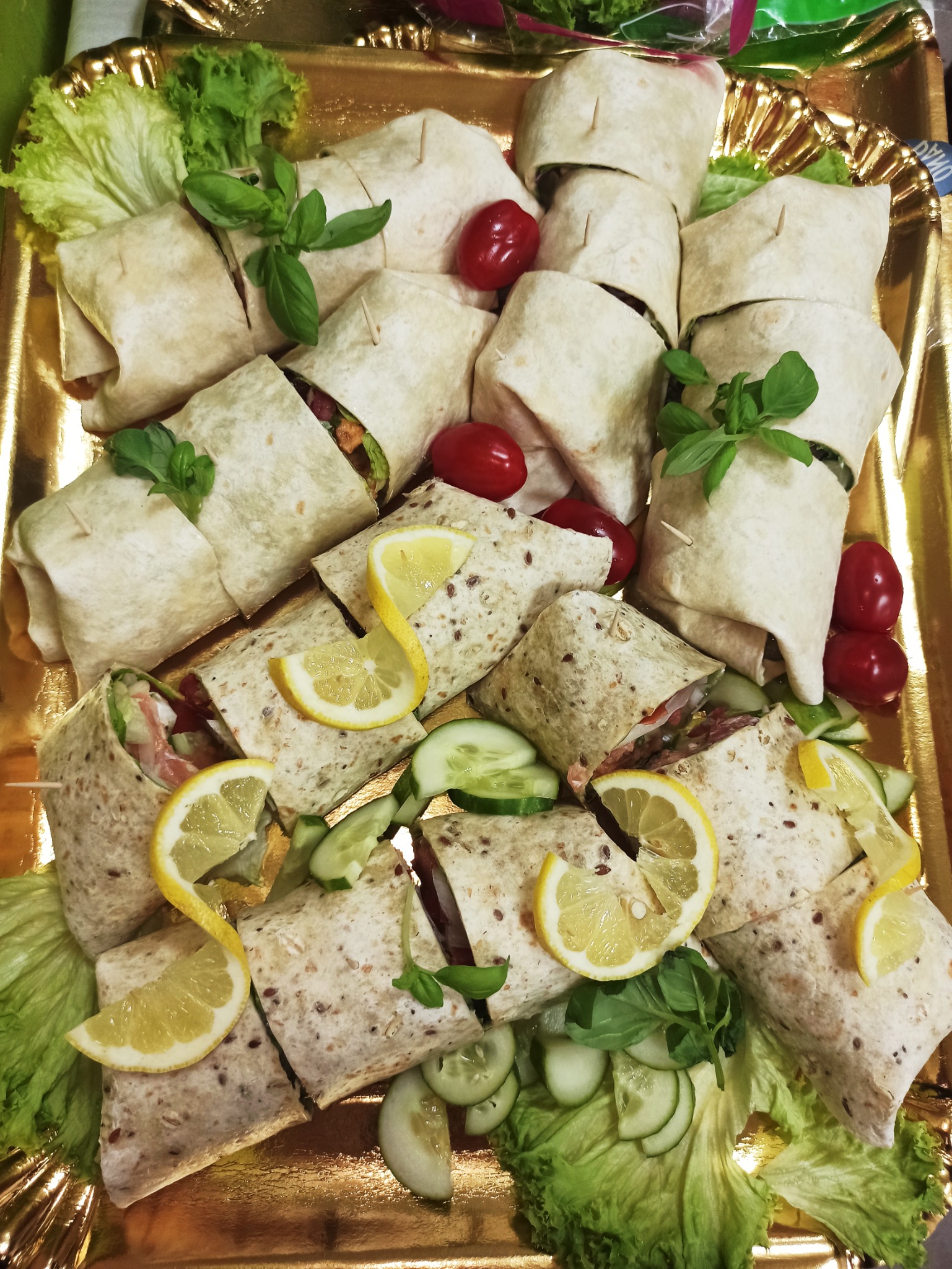 Tortille z różnymi nadzieniami, udekorowane plasterkami cytryny, bazylią, pomidorkami cherry i ogórkiem, ułożone na złotej tacy.