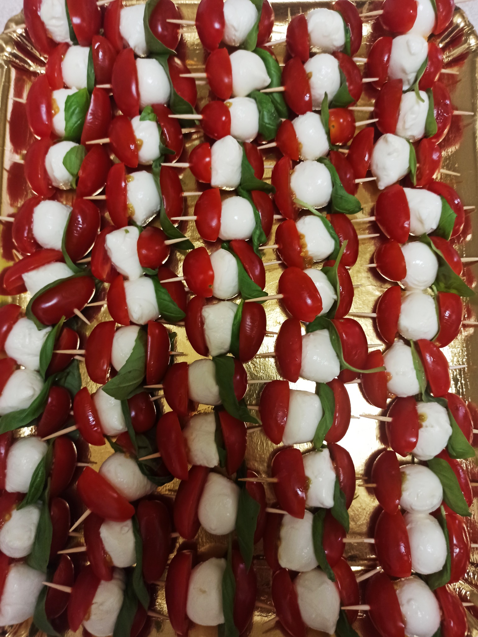 Szczecińskie koreczki Caprese na złotym paterze: pomidorki cherry, kulki mozzarelli i listki bazylii, elegancko nabite na szpadki.