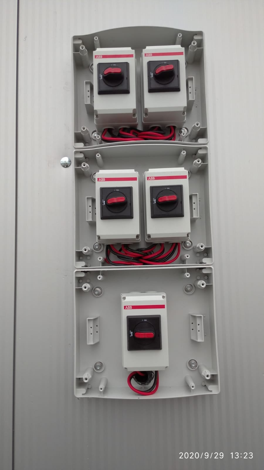 Panel elektryczny z trzema rzędami wyłączników firmy ABB, z widocznymi przewodami czerwonymi i czarnymi, zamontowany na szarej ścianie.