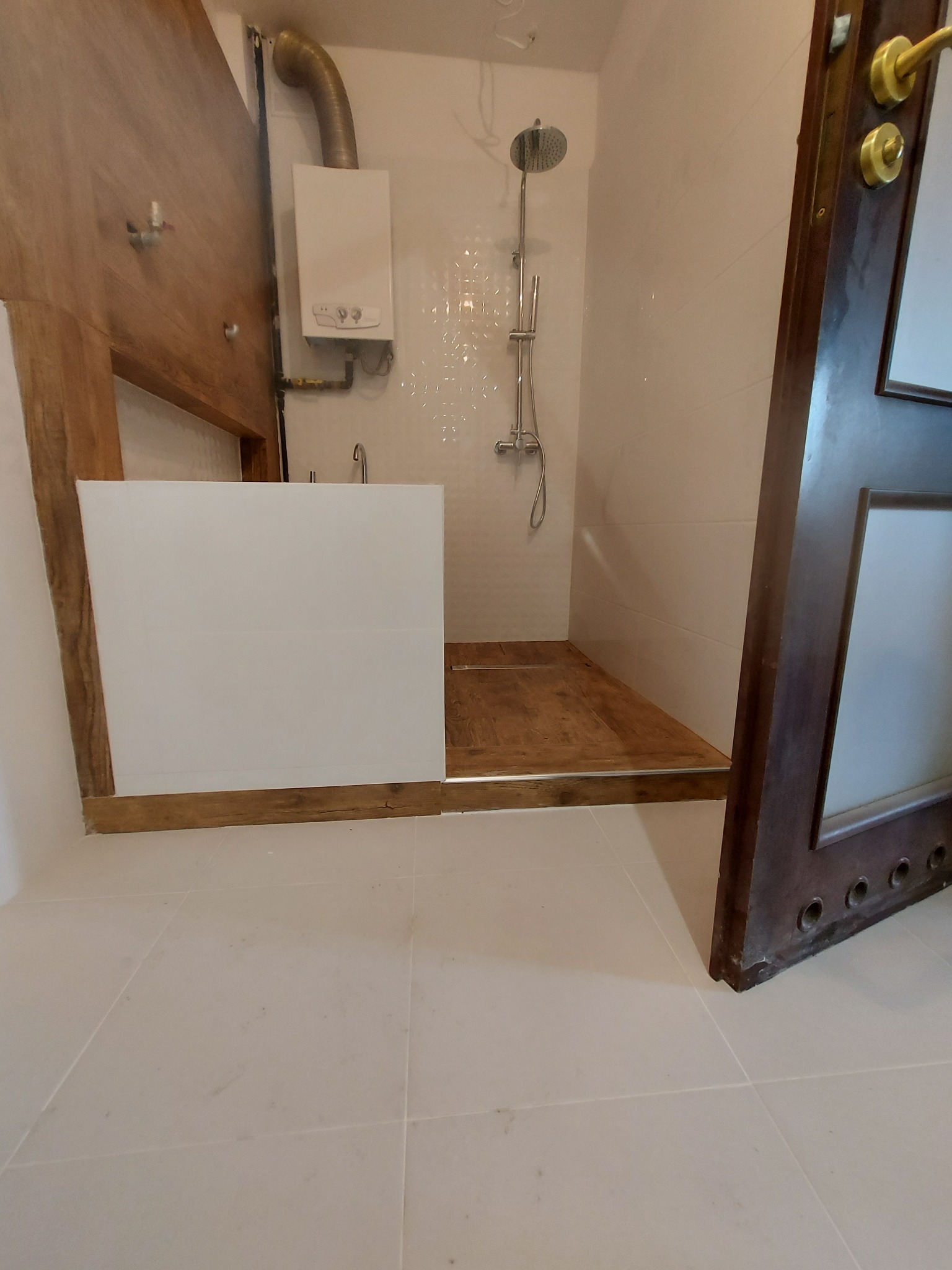 Wykończona łazienka z drewnianym podestem prysznicowym i obudową wanny, widoczny bojler i bateria prysznicowa.