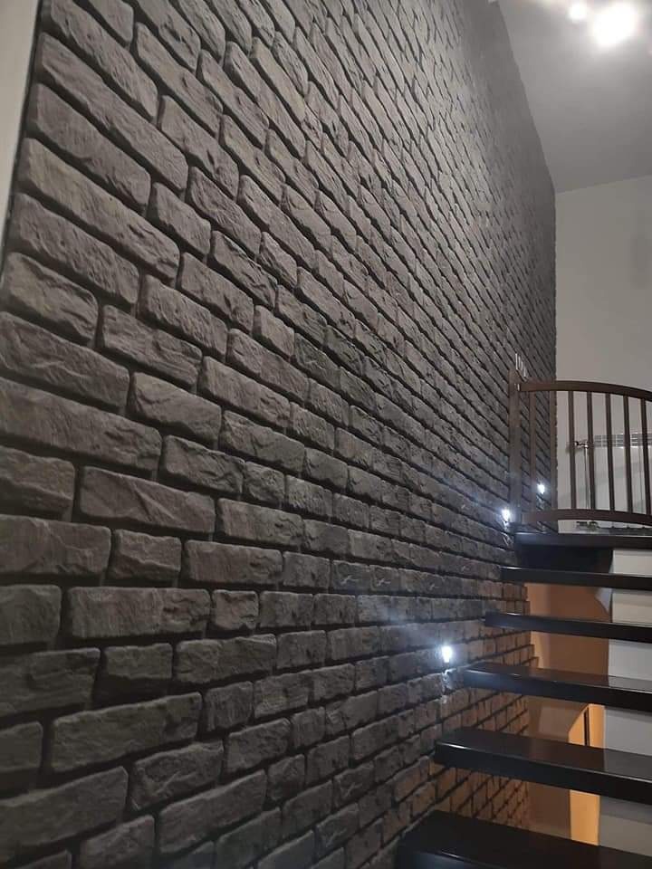 Dekoracyjna ściana z szarej cegły przy schodach z podświetleniem punktowym.