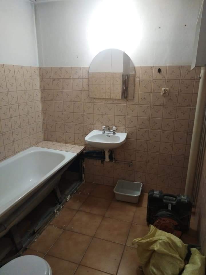 Łazienka w trakcie demontażu: widoczna wanna, umywalka, częściowo zdjęte płytki, narzędzia w kufrze i wiadro na podłodze, przygotowania do remontu.