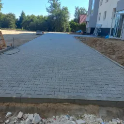 Ułożona szara kostka brukowa na podjeździe przed budynkiem, widoczne obrzeża i przygotowany teren pod dalsze prace.