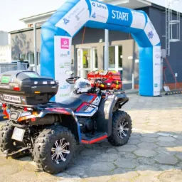 Quad ratowniczy z wyposażeniem medycznym, zaparkowany przed budynkiem z bramą startową, widoczne logo firmy medycznej na pojeździe.