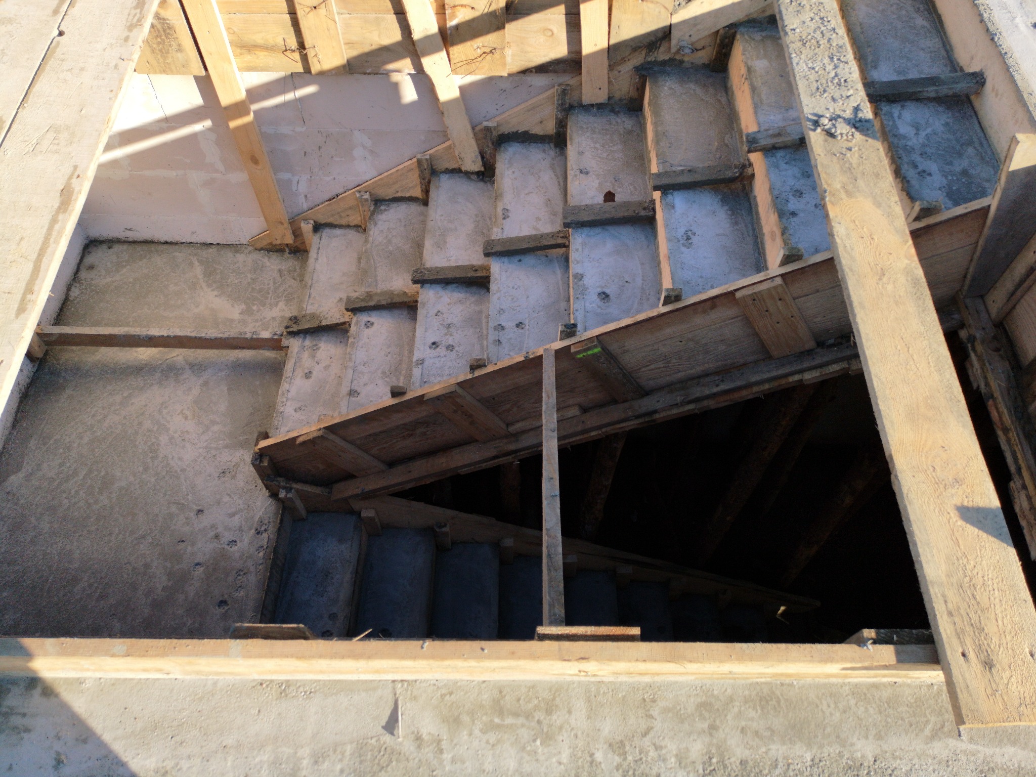 Surowe betonowe schody w trakcie budowy w Grodzisku Mazowieckim, widok z góry, z widocznym szalunkiem i drewnianą konstrukcją wsporczą.