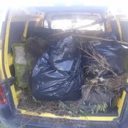 Żółty furgon z otwartymi drzwiami bagażnika, załadowany workami na śmieci, gałęziami i zielonymi odpadami roślinnymi.