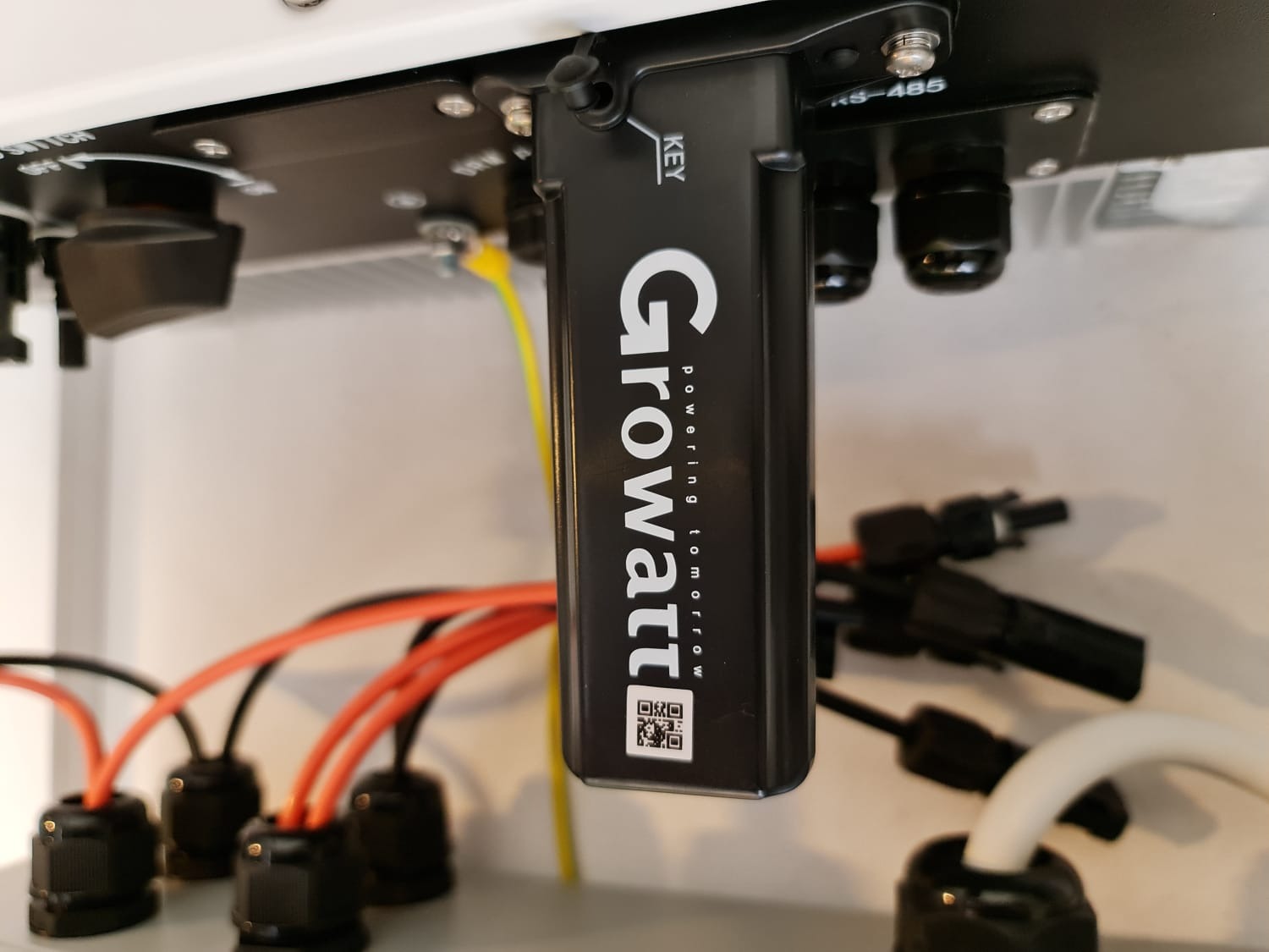 Szczegółowe ujęcie modułu Growatt z widocznymi kablami, złączami i elementami montażowymi, z bliska widoczny kod QR i napis 'Powering tomorrow'.