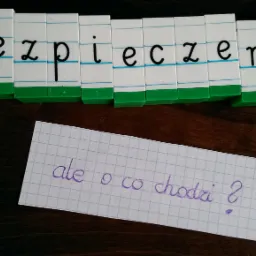 Napis 'Ubezpieczenia' ułożony z klocków na biurku obok kartki z pytaniem 'ale o co chodzi?'