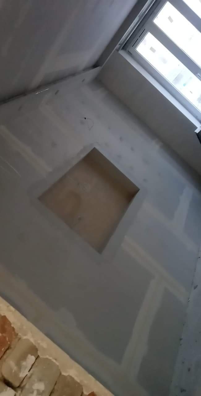 Ściana w trakcie prac wykończeniowych z wnęką, widoczne ślady szpachlowania i przygotowania pod gładzie, fragment muru z cegieł w dolnym rogu.