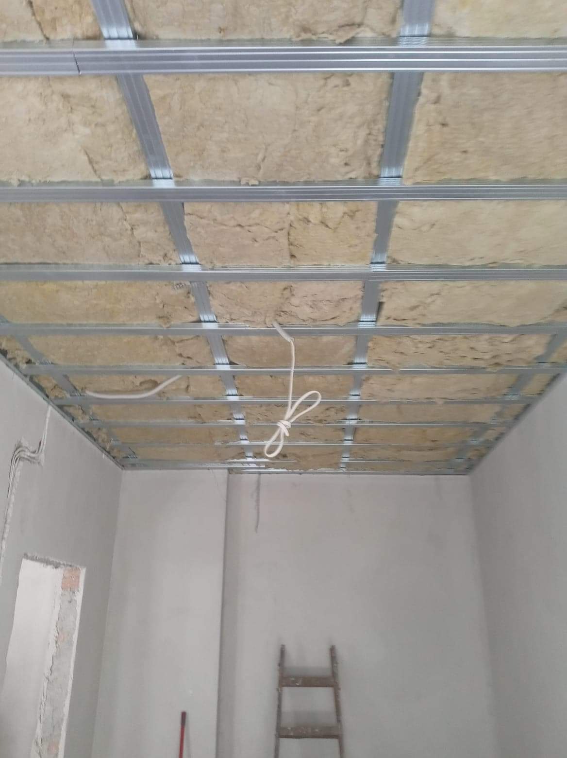 Sufit podwieszany w trakcie prac izolacyjnych wełną mineralną, widoczne metalowe profile konstrukcyjne, Szczecin.