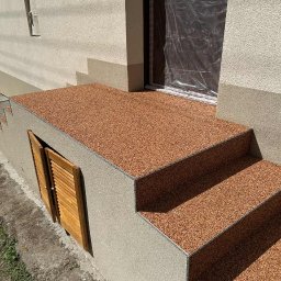 Vladyslav Fedortsov Alternatywa - Wykończone schody wejściowe z żywicy epoksydowej w kolorze brązowym, z widocznymi detalami wykończenia i fakturą. Drzwi zabezpieczone folią ochronną.