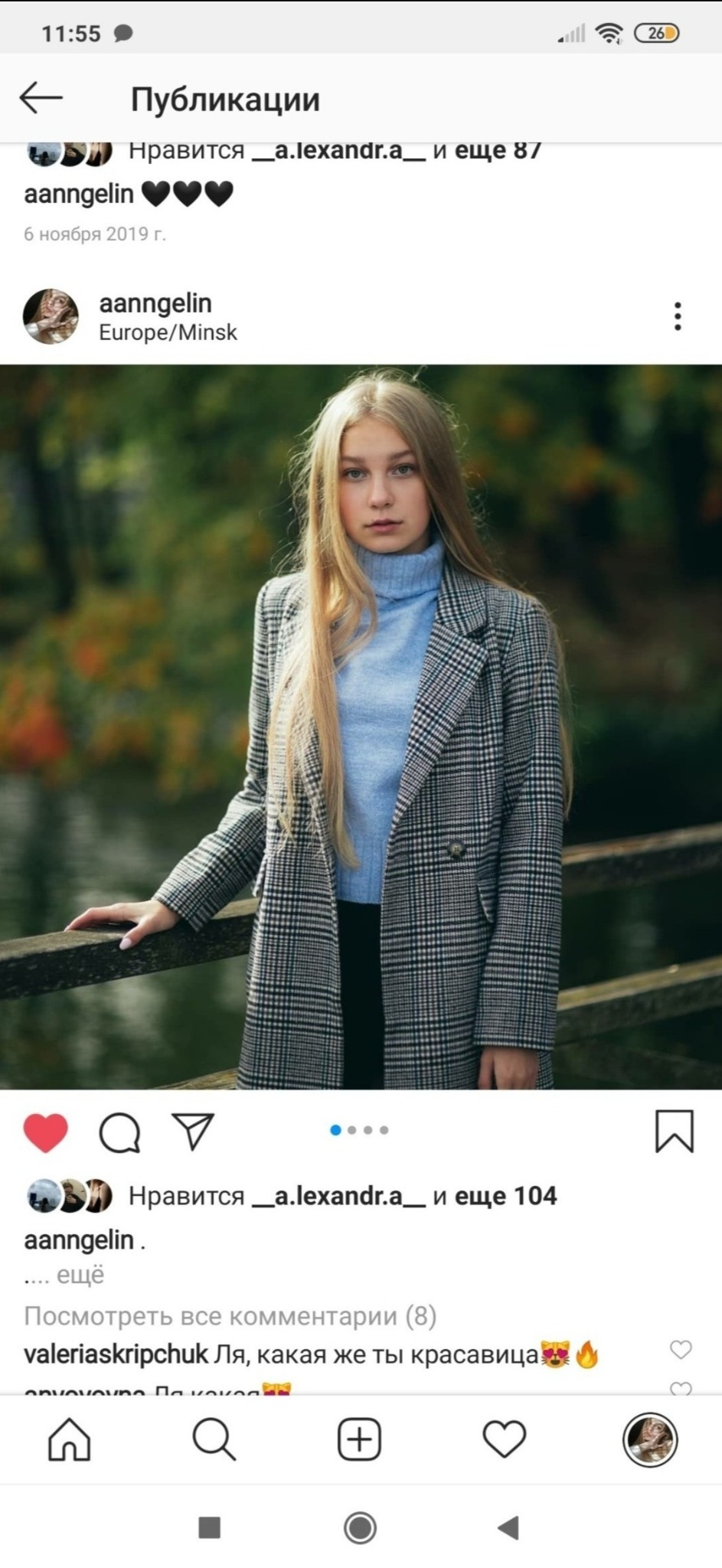 Portret młodej kobiety w płaszczu w kratę i błękitnym golfie, opierającej się o drewnianą barierkę na tle jesiennego krajobrazu.