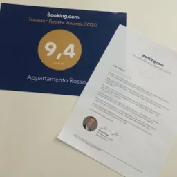 Booking.com Traveller Review Awards 2020: Dyplom z oceną 9.4/10 dla Appartamento Rosso oraz list gratulacyjny od Booking.com, leżące na jasnym tle.