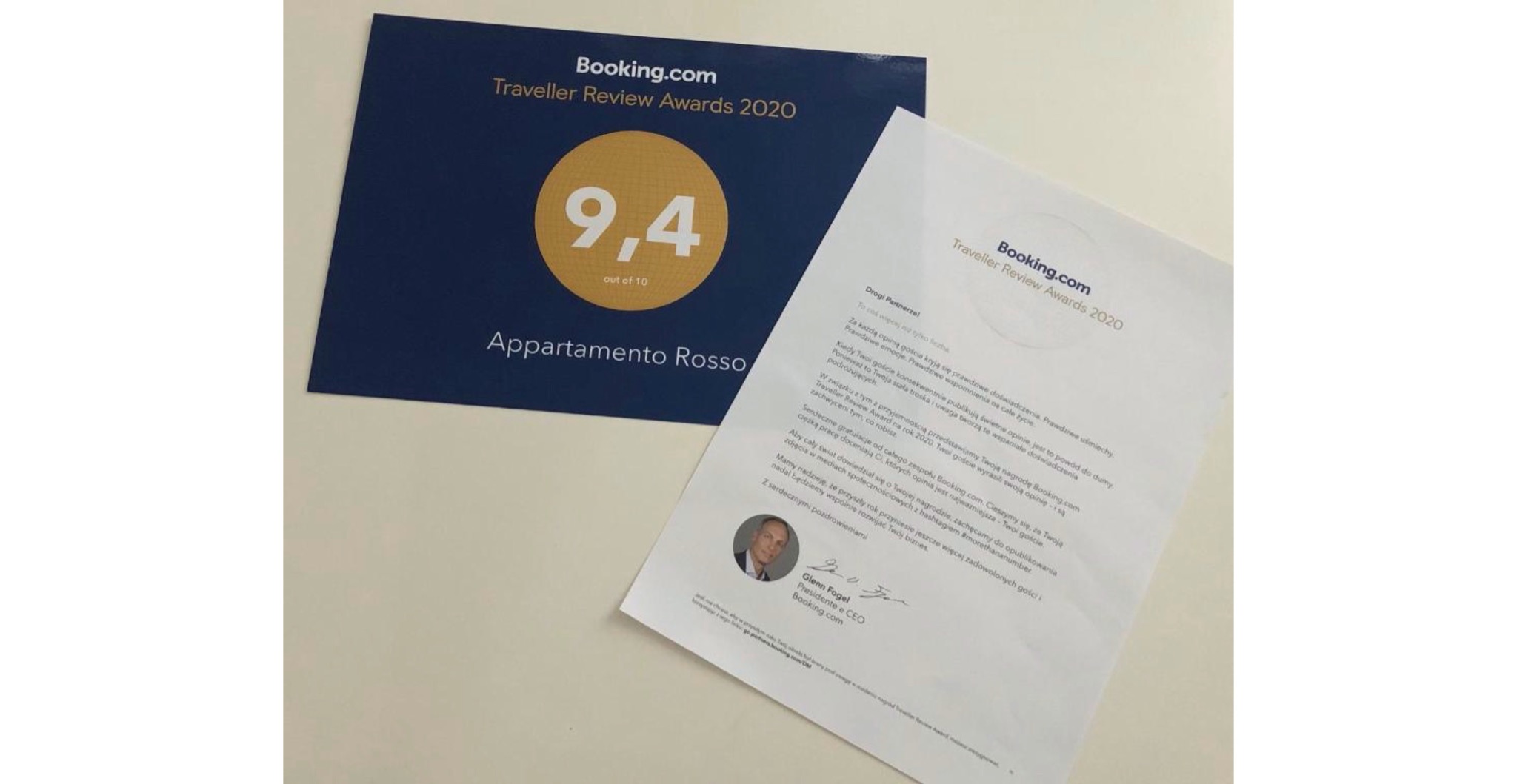 Booking.com Traveller Review Awards 2020: Dyplom z oceną 9.4/10 dla Appartamento Rosso oraz list gratulacyjny od Booking.com, leżące na jasnym tle.