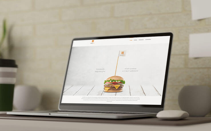 Laptop wyświetla stronę internetową z burgerem i logo Brandpick na fladze. Minimalistyczny design, stonowana kolorystyka, nowoczesny wygląd strony.