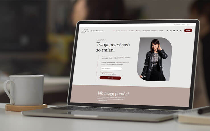 Laptop wyświetla stronę internetową z wizerunkiem kobiety i tekstem 'Twoja przestrzeń do zmian'. Obok stoi biały kubek.