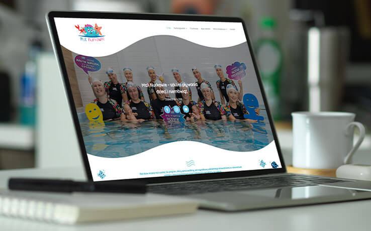 Ekran laptopa prezentuje stronę internetową szkoły pływania 'Mali Nurkowie' z uśmiechniętymi instruktorami i dziećmi w wodzie. Obok notatnik i kubek.