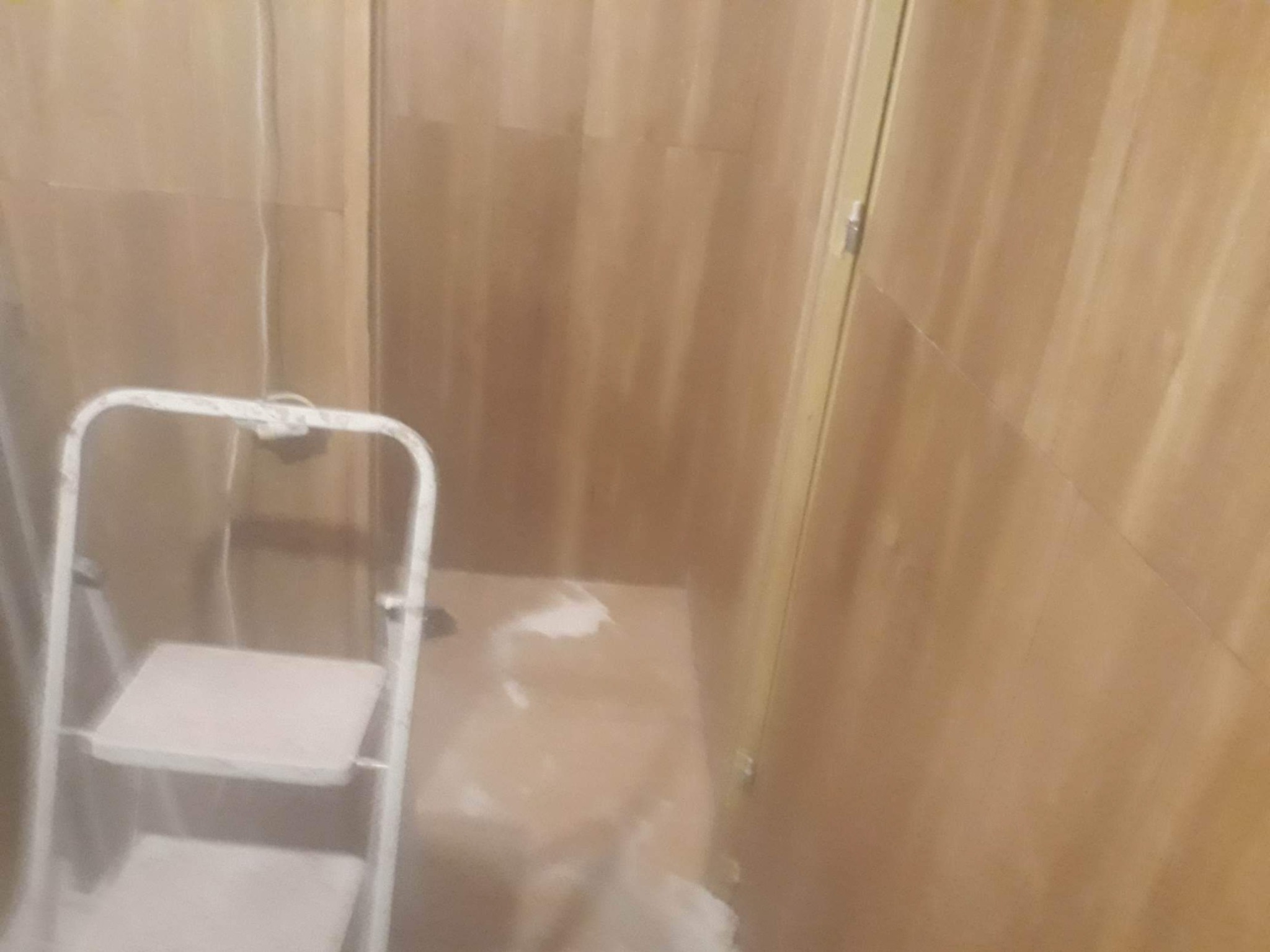 Wnętrze pomieszczenia z drewnianą boazerią, biała drabina malarska stoi w rogu, widoczne ślady białej farby na podłodze.