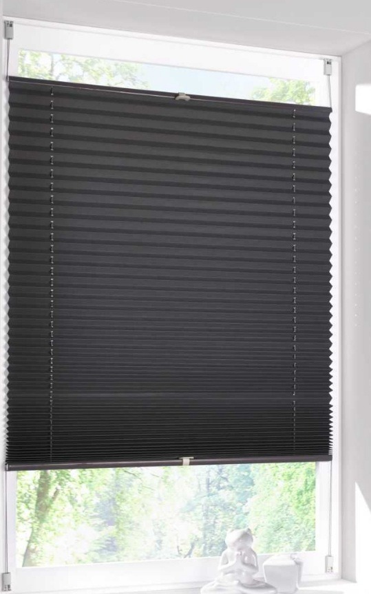 Ciemnoszara plisa okienna zamontowana w białej ramie okiennej z widokiem na zieleń za oknem. Na parapecie biała figurka dekoracyjna.